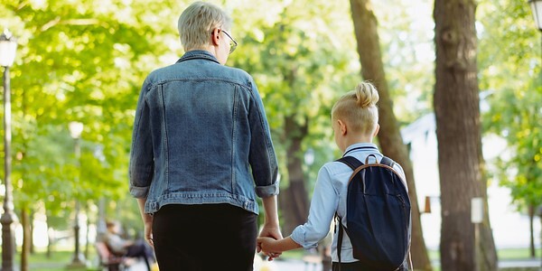 mother and son going to school holding hands. Caucasian blond boy with hairs tied up in ponytail looking at mom. Image with seective focus